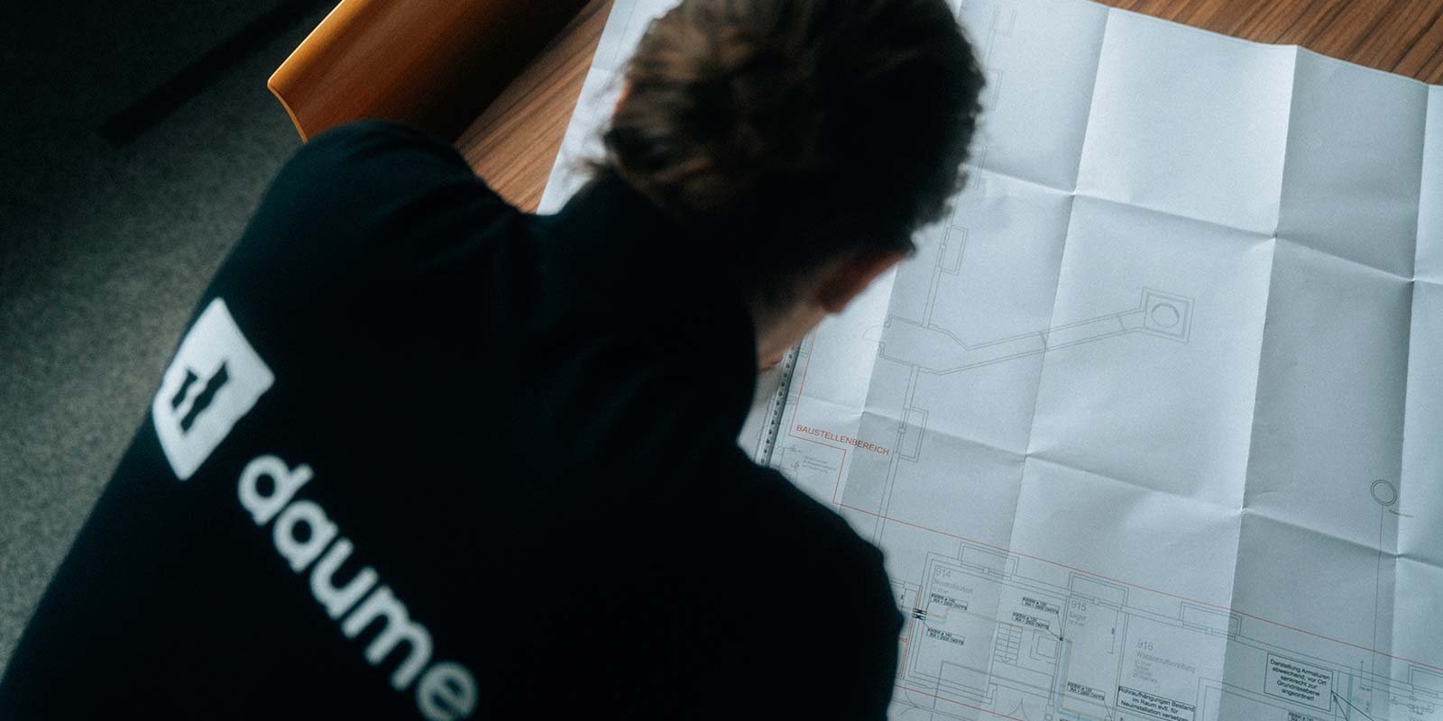 Der Bauplan zeigt detaillierte Zeichnungen eines Baustellenbereichs, während die Person konzentriert darüber nachdenkt.